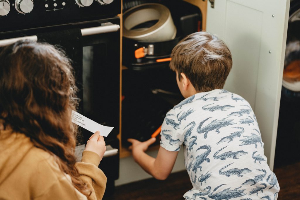 One child goes through the pot cupboard while the other reads from a slip of paper. 