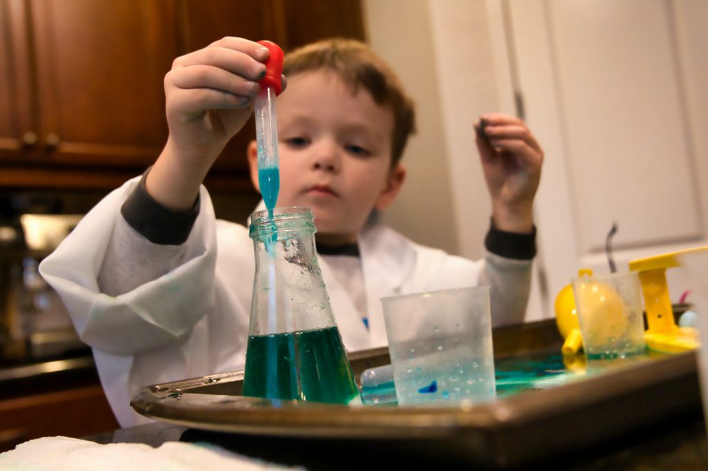 Young boy in a lab coat adding blue liquid to a beaker