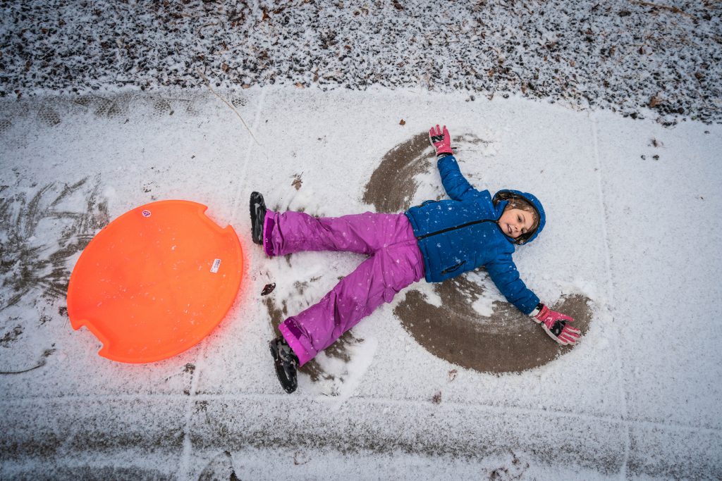 Child doing snow angels next to an orange sled